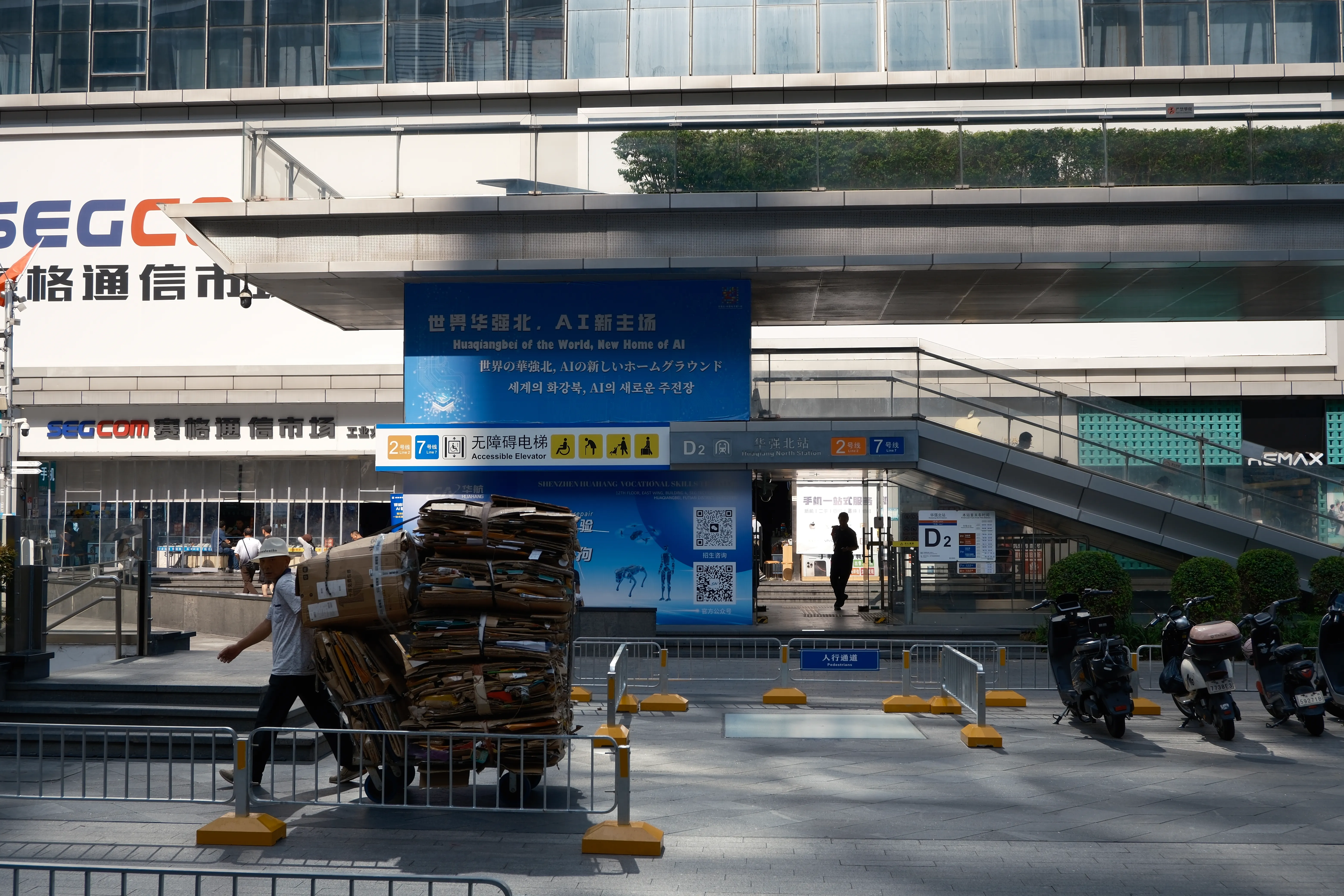 A man pushes a cart piled high with flattened cardboard past the SEG electronics market, under a blue banner reading "Huaqiangbei of the World, New Home of AI"